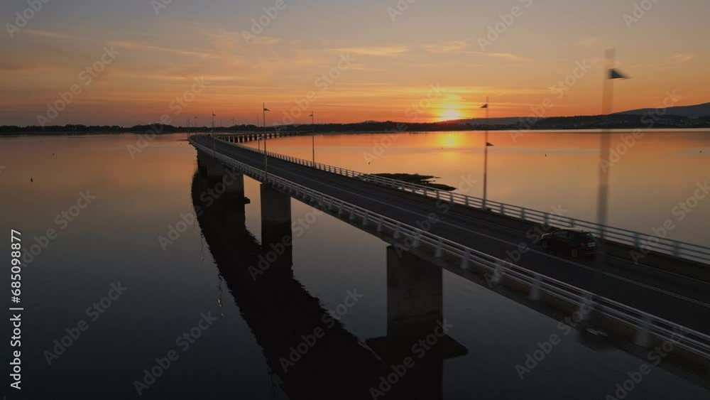 Establishing aerial view of a cars driving on a long sea bridge at sunset with a beautiful golden color reflect of the sea. Concept of transportation and travel in Spain Arosa Island Bridge Establishing aerial view of a cars driving on a long sea bridge at sunset with a beautiful golden color reflect of the sea. Concept of transportation and travel in Spain Arosa Island Bridge