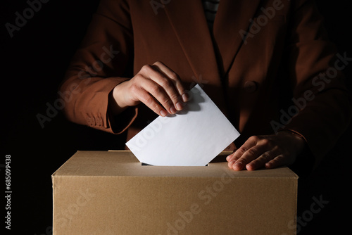 Paper voting box with form and men on black background, close up © Atlas
