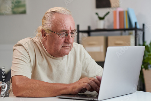 Concentrated senior man in glasses working on laptop at home