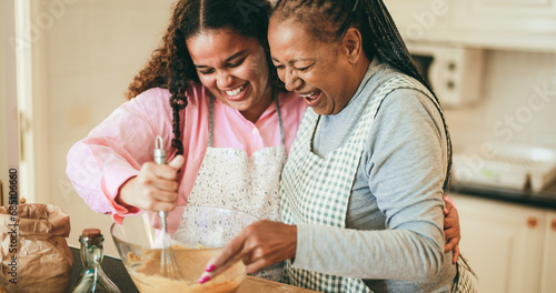 African mother and daughter having fun preparing fruit cake at home - Winter holidays and family concept - Soft focus on senior woman mouth