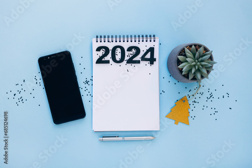 New year resolutions 2024 concept. 2024 goals list with notebook, pen, plant and phone on table. Resolutions, plan, goals, action, checklist, idea concept photo
