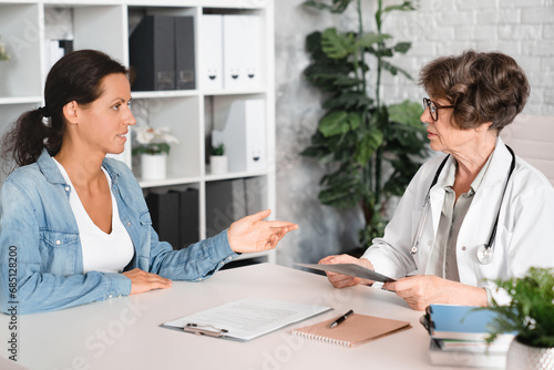 Female middle-aged patient complaining about illness diseases symptoms to elderly senior doctor general practitioner gynecologist in hospital