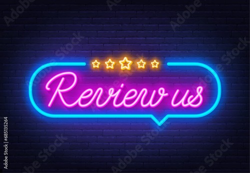 Review Us neon sign in the speech bubble on brick wall background.