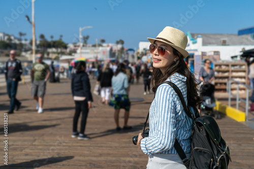 pretty stylish asian Chinese female backpacker having fun looking around at santa monica pier. travel lifestyle and spring holiday in united states