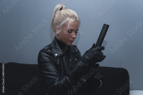A girl in black leather with a pistol with a silencer in a room with low lighting. photo