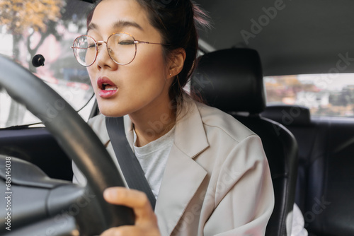 Front view of Asian Thai woman asleep and sleepy, closing eyes while driving a car on road, insurance concept. © Suthida