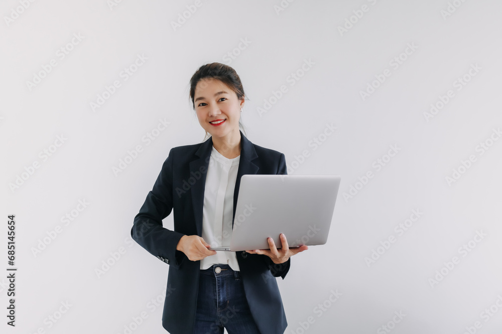 Asian Thai woman wear blazer suit, smiling looking at camera and holding laptop, presenting notebook with happy face, standing isolated over white background wall. Asian Thai woman wear blazer suit, smiling looking at camera and holding laptop, presenting notebook with happy face, standing isolated over white background wall.
