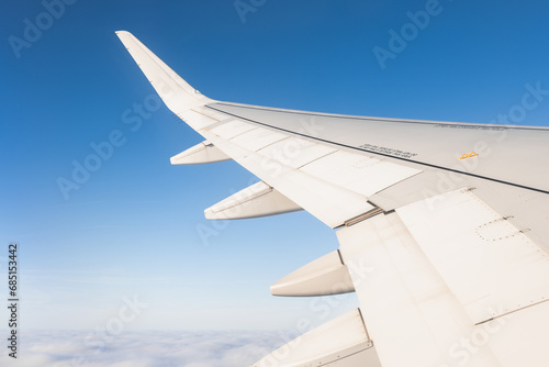 Crop wing of aircraft flying over white clouds against blue sky on sunny weather photo