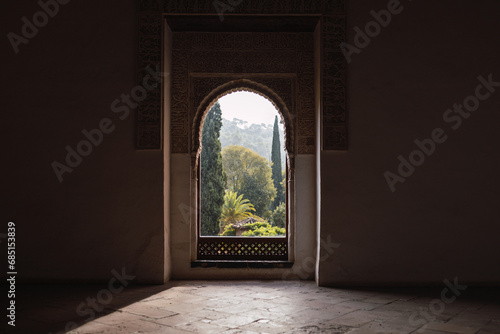 Lush garden seen through arached window in dark room of historic Alhambra fortress in Granada, Spain photo