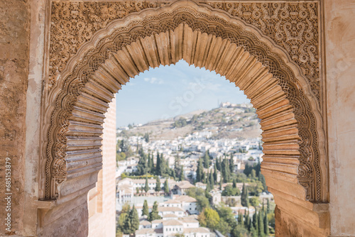 Arch window of Alhambra fort with blurred residential buildings and trees in the background photo