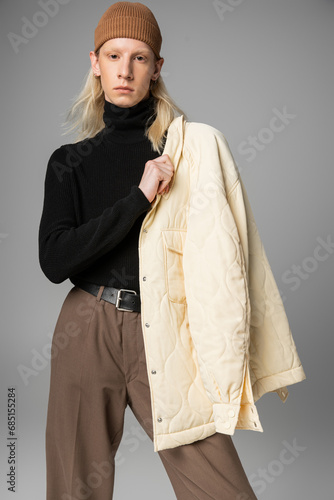 good looking non binary model posing with stylish winter jacket on shoulder and looking at camera photo