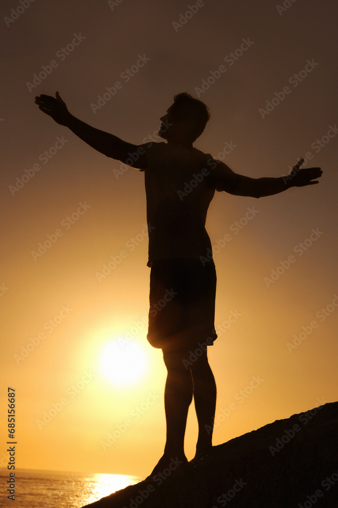 Fototapeta premium Silhouette, man and stretching with hands for yoga, health and wellness on beach with sunset and zen. Person, shadow and pilates or sunrise for balance, mindfulness and healthy body by ocean or sea