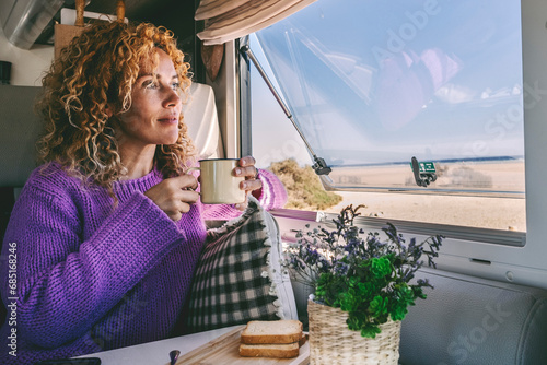 One woman alone inside camper van motorhome admiring outdoors scenic parking and drinking tea in relax leisure indoor activity. Travel people for vacation and lifestyle van life off grid. Phone table