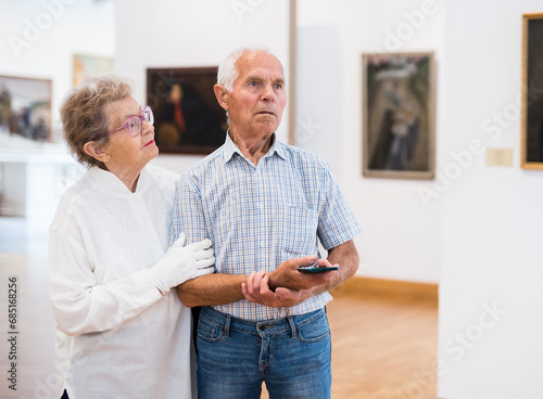 Mature European couple examines paintings in an exhibition in hall of art museum photo