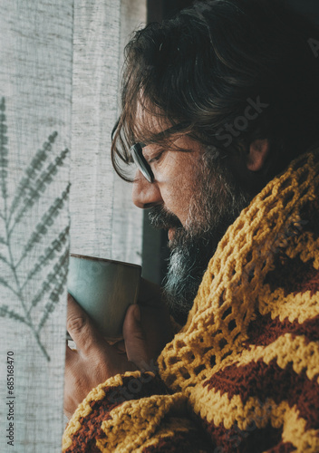 One man drinking hot drink at home covered with woolen cover. Concept of cold temperature at home and flu syptoms. Coronavirus or influenza bad health condition. People and winter indoor house photo