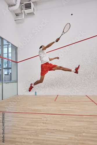 motion shot, active african american player holding racquet while jumping and playing squash