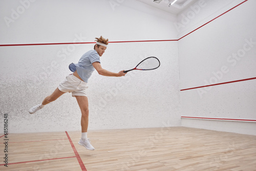 motion shot, energetic player holding racquet and jumping while playing squash inside of court