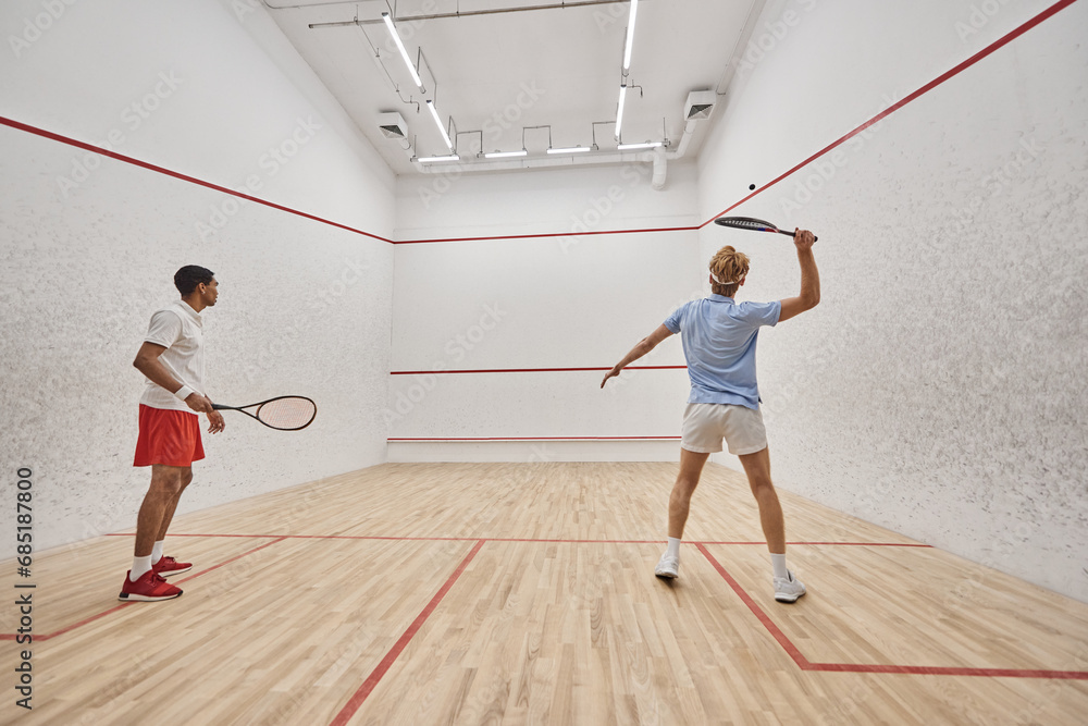 active and interracial friends playing squash together inside of court, preparing for competition active and interracial friends playing squash together inside of court, preparing for competition