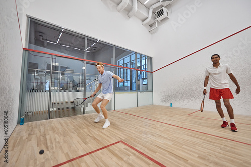 dynamic interracial sportsmen playing squash together inside of court, challenge and motivation