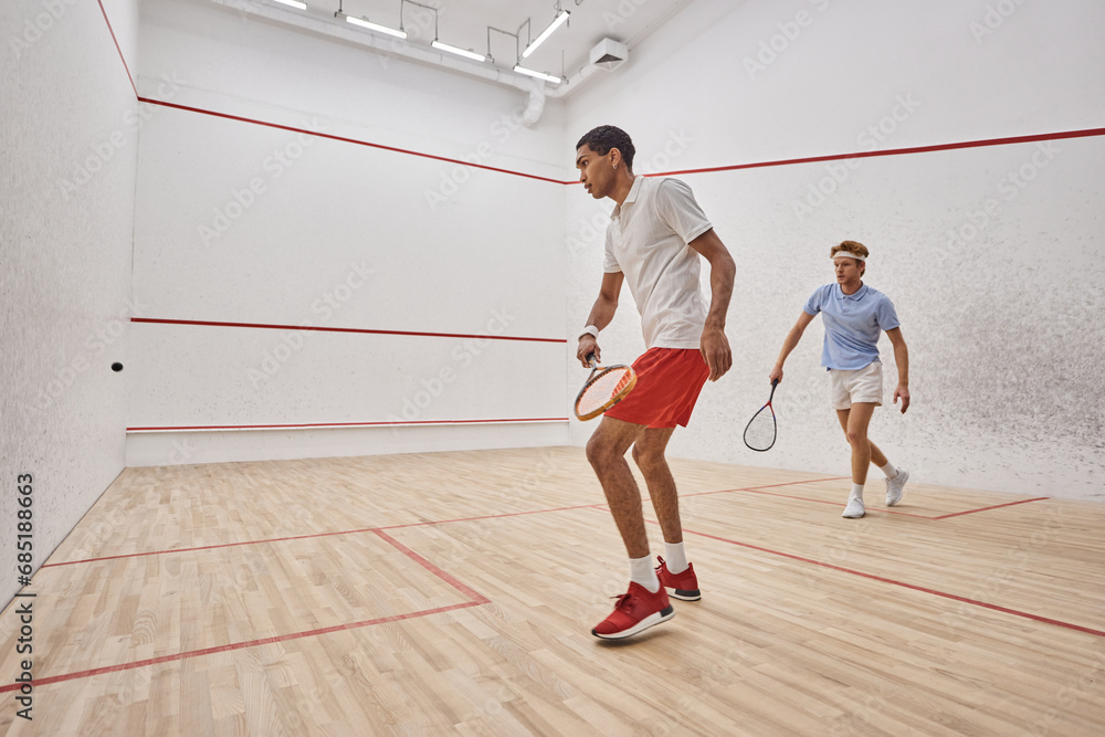 young and active interracial men playing squash inside of court, challenge and motivation