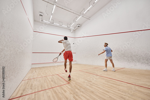interracial players in sportswear playing squash together inside of court, fitness and motivation © LIGHTFIELD STUDIOS