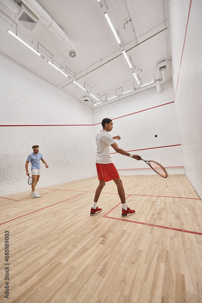 young interracial sportsmen playing squash together inside of indoor court, motivation and sport