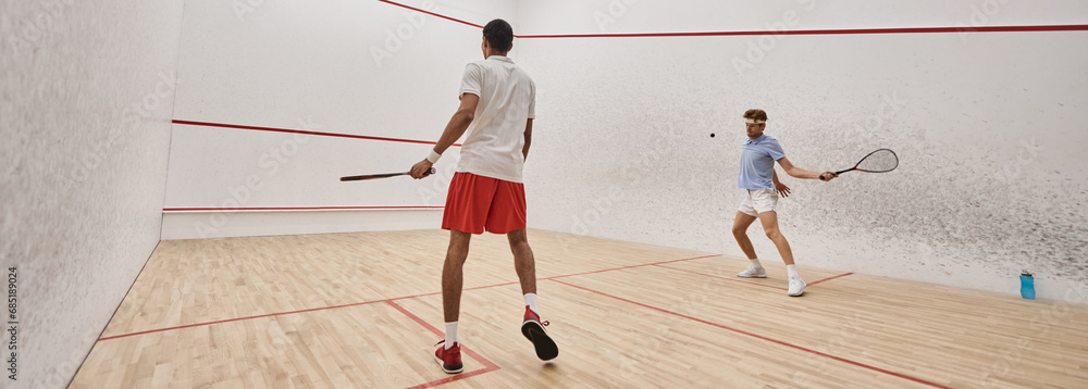 interracial athletic men in sportswear playing squash together inside of court, motivation banner