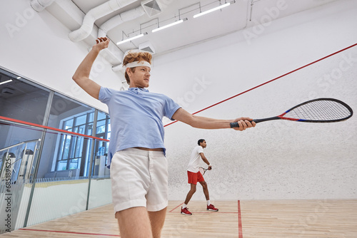 interracial players in sportswear playing squash together inside of court, energetic lifestyle © LIGHTFIELD STUDIOS
