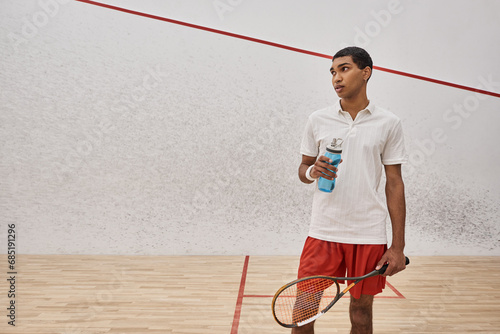 athletic african american sportsman holding bottle of water and racquet after playing squash © LIGHTFIELD STUDIOS