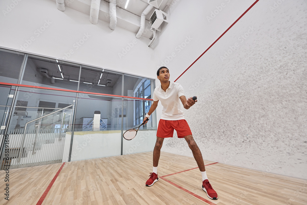 fit african american sportsman holding squash ball and racquet while playing game inside of court