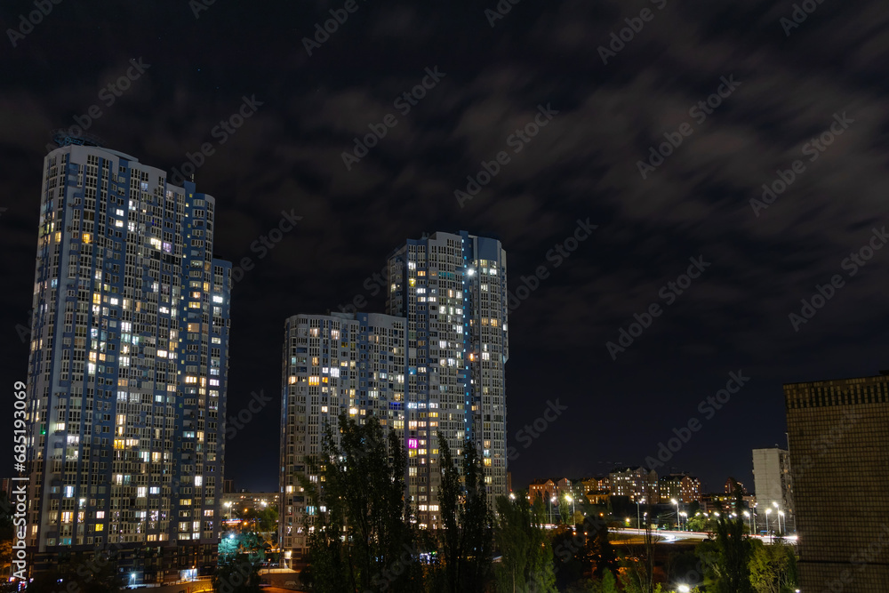 Evening cityscape with high multi-storey residential buildings. Light from the windows of modern buildings in the city on a summer night