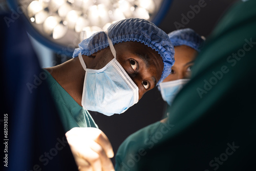 Diverse male and female surgeons with face masks doing surgery in hospital operating room photo