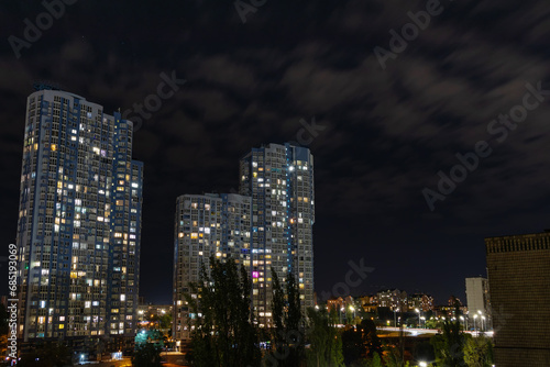 Evening cityscape with high multi-storey residential buildings. Light from the windows of modern buildings in the city on a summer night