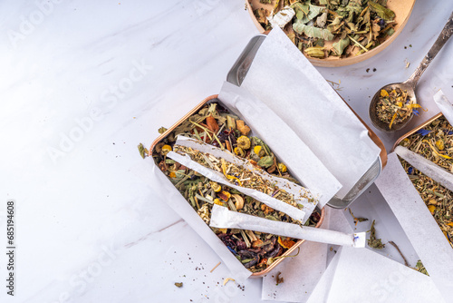 Alternative healthy herbal smoking blend. Handmade craft cigarette, preparation process, with mixture of herbs, leaves and flowers, with boxes, paper, on white background photo