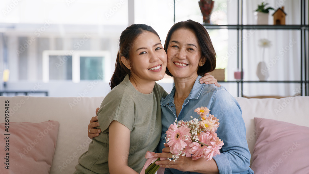 Happy time Mother day grown up child girl looking at camera cuddle hug give flower bouquet gift to mature mum. Love kiss care mom asia middle age adult people smile enjoy relax sitting at home sofa. Happy time Mother day grown up child girl looking at camera cuddle hug give flower bouquet gift to mature mum. Love kiss care mom asia middle age adult people smile enjoy relax sitting at home sofa.