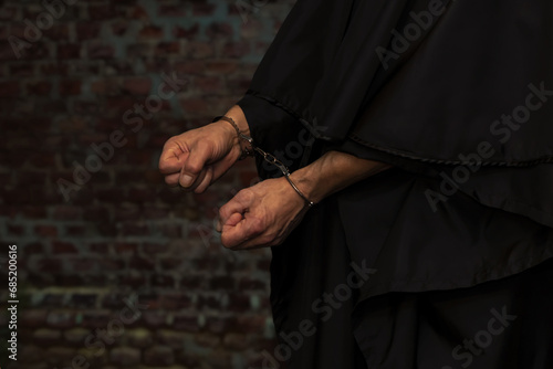 The hands of a monk or priest in handcuffs on the background of a stone wall. Concept: old criminal, criminal liability, religious figure. photo