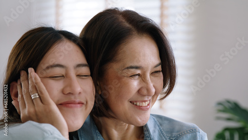 Happy time May Mother day cuddle hug care love face to face kiss cheek to mature mum. Asia middle aged old mom adult people smile enjoy receive gift flower from young child sitting at home sofa relax. © ChayTee