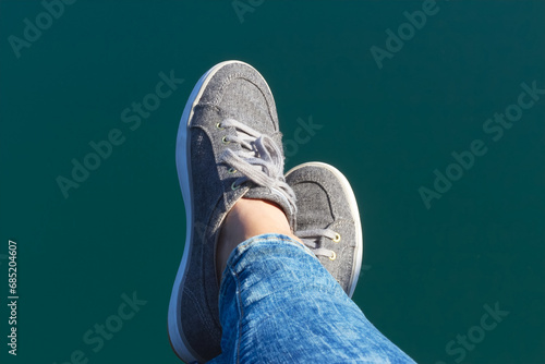 Woman's feet in canvas sneakers above blue water surface background. Summer vibes. Relaxation concept. photo