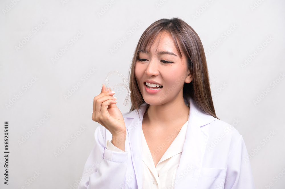 Young female dentist holding invisalign braces over white background studio, dental healthcare and Orthodontic concept. Young female dentist holding invisalign braces over white background studio, dental healthcare and Orthodontic concept.