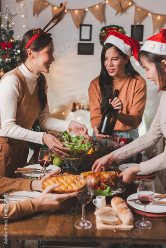 Group of young adult Asian Friends holiday party dinner at home around the table. Celebrate Christmas. People arranging food preparing dinner talk and laugh with joy in Christmas eve night.