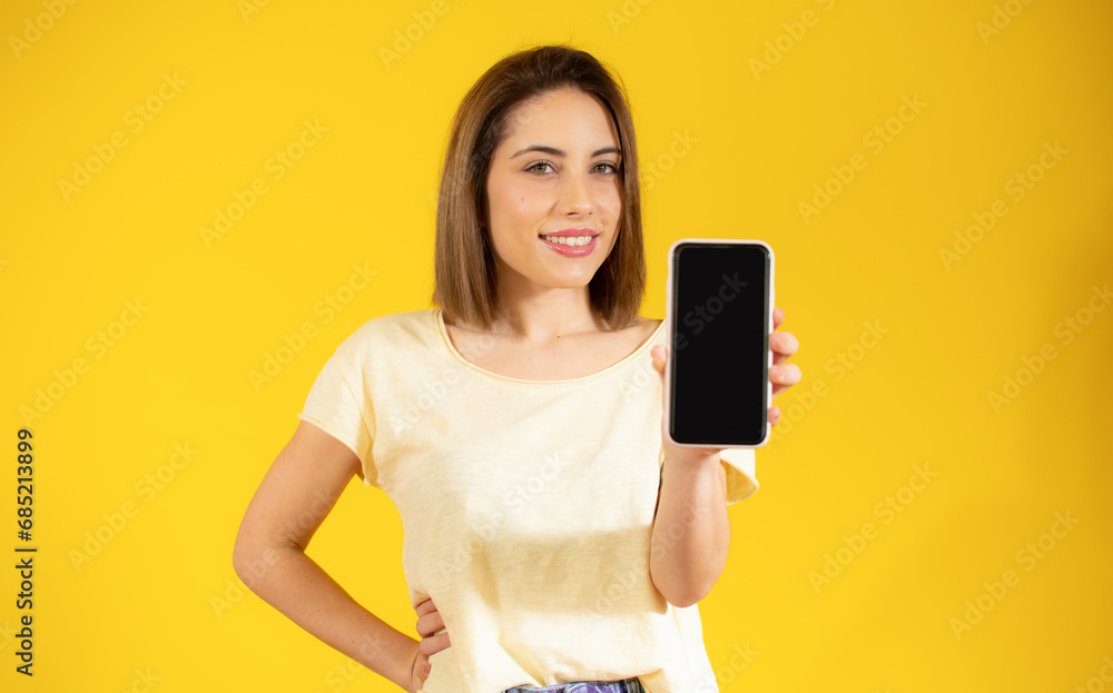 Image of pretty young woman isolated over yellow background. Looking camera showing display of mobile phone. Image of pretty young woman isolated over yellow background. Looking camera showing display of mobile phone.