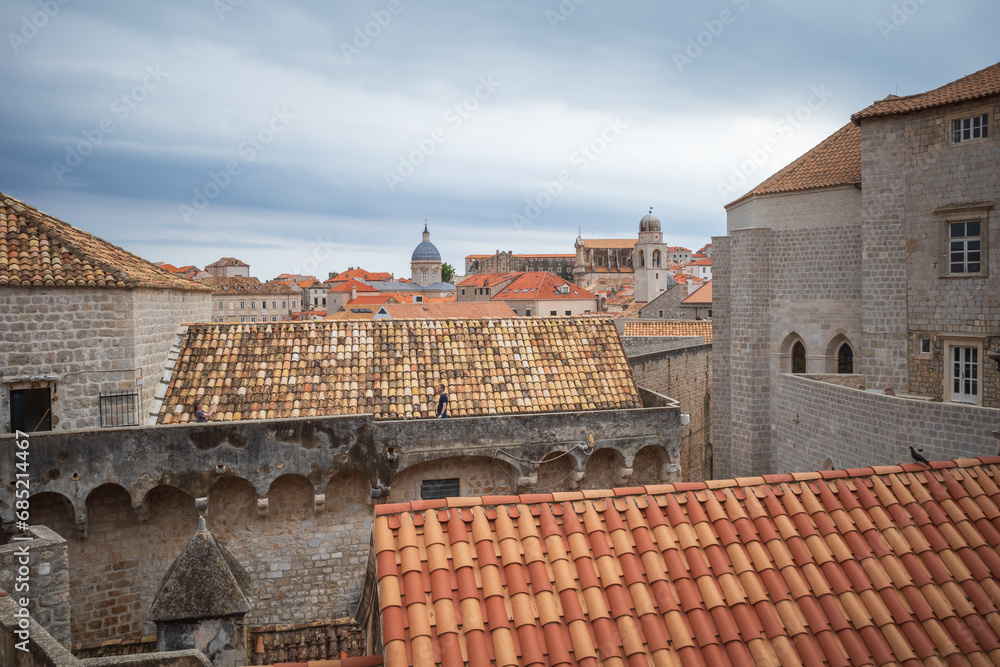 View to the red roofs of Dubrovnik Old town on cloudy summer day. Tourists walking on the walls of city