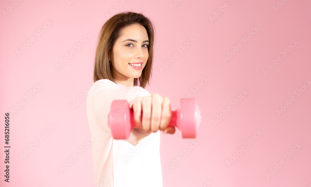 Beautiful young woman holding dumbbell isolated over pink background. Beautiful young woman holding dumbbell isolated over pink background.