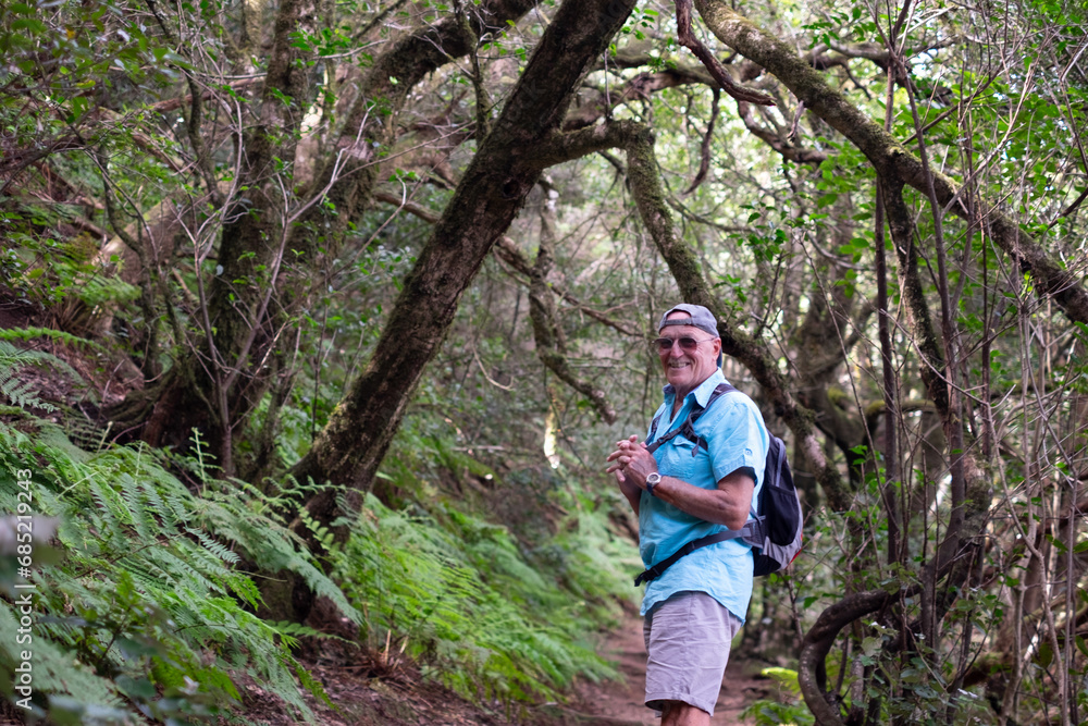 Trekking day in the forest for a happy senior man looking at camera smiling enjoying nature and healthy lifestyle in vacation or retirement