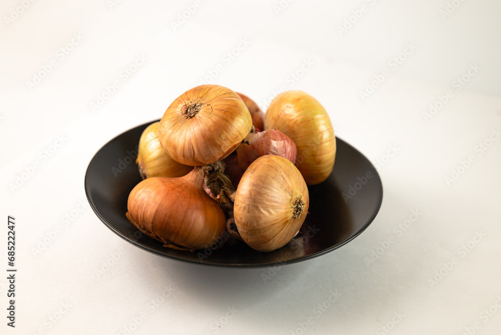 Obraz premium Onions are piled on a black plate on a white background