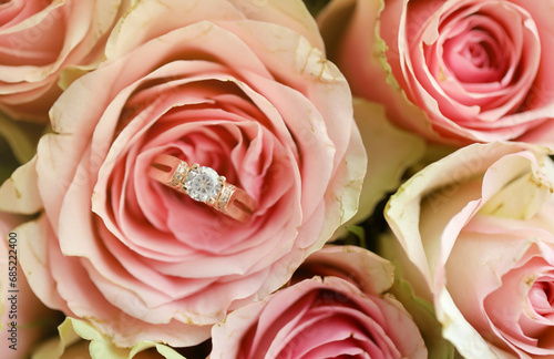 Gold diamond engagement ring in beautiful pink rose flower among big amount of roses in big bouquet close up with blurred background photo
