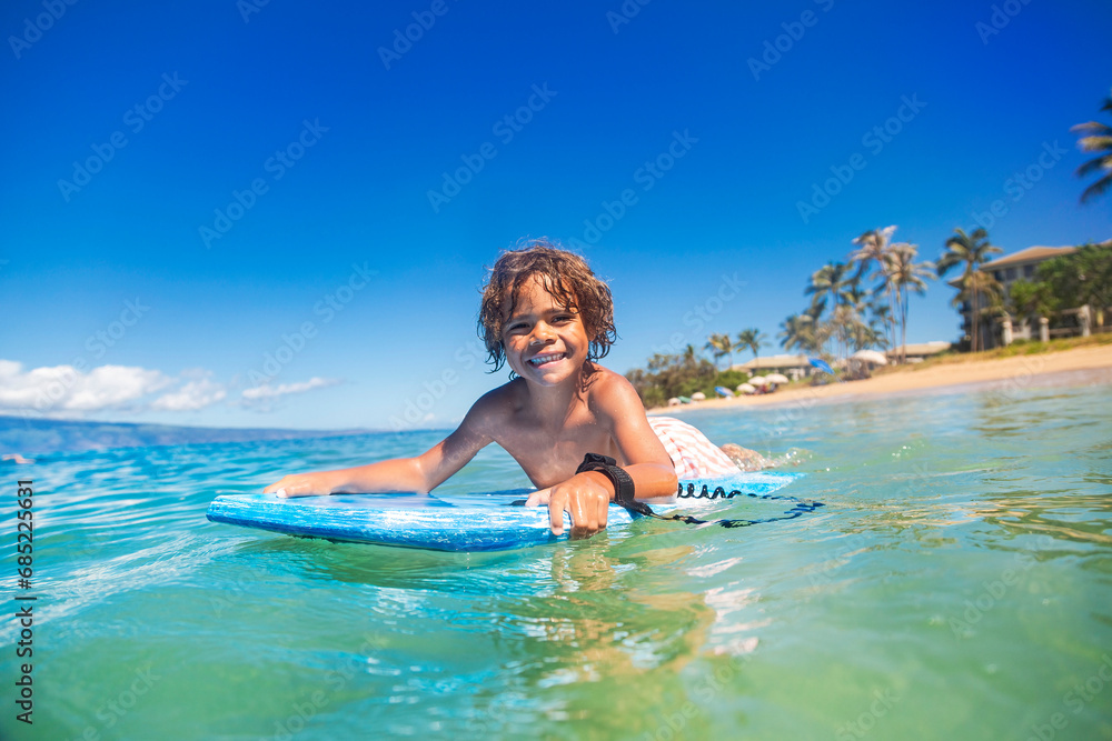 Smiling diverse young boy boarding in the beautiful blue ocean. Enjoying a fun day playing at the beach while on vacation in Hawaii