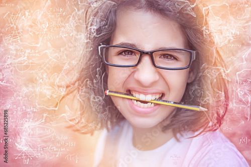 Portrait of a schoolgirl fed up with holding a pencil between her teeth photo