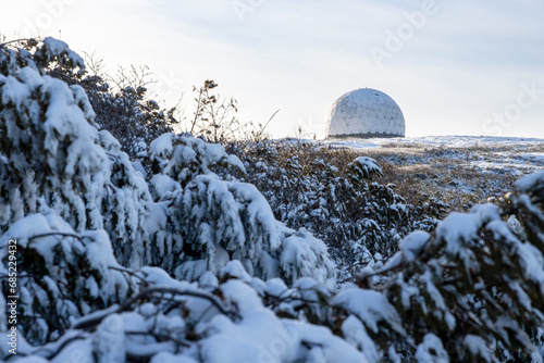 The white dome (radiotransparent shelter) of an abandoned radar station on the top of a mountain. In the foreground are snow-covered branches of a dwarf cedar tree. Magadan region, Russia. © Andrei Stepanov