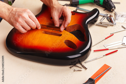 Guitar repairer measures size of holes for tremolo in body of guitar with ruler.